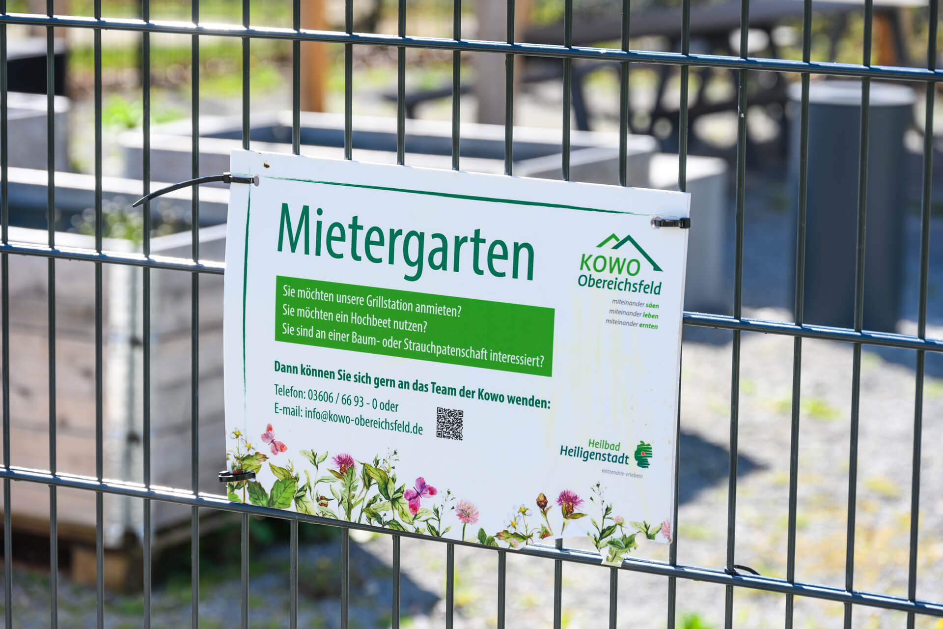 Schild „Mietergarten" der KOWO Obereichsfeld am Zaun in Heilbad Heiligenstadt mit Infos zu Hochbeet und Grillstation